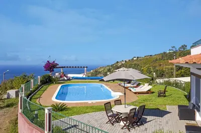 a swimming pool with chairs and an umbrella and the ocean at Villa Theos House by Villa Plus in Fajã da Ovelha