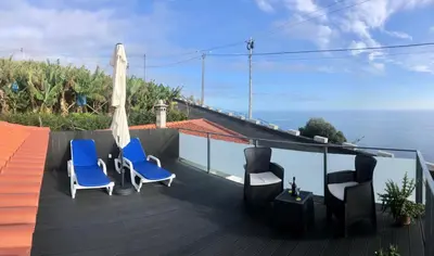 a deck with chairs and an umbrella and the ocean at Casa Miradouro do Pigarro, Sunny Apartment in Calheta