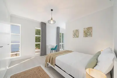 a white bedroom with a bed and a blue chair at Intelsol Calheta Apartments by An Island Apart in Calheta