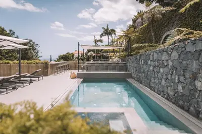 a swimming pool with a stone wall next to a stone wall at QUINTA TORRINHA LUXODREAM Apartment in Funchal