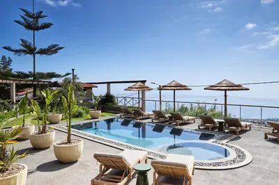 a swimming pool with chairs and umbrellas on a resort at Yeotown Madeira Wellness Hotel and Nature Stay in Arco da Calheta