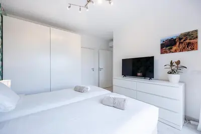 a white bedroom with two beds and a flat screen tv at Villa Sagres Surf in Sagres