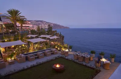an outdoor restaurant with a view of the ocean at night at La Villa at The Cliff Bay - PortoBay in Funchal