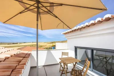 a patio with a wooden table and an umbrella at Casa Monte Salema in Vila do Bispo