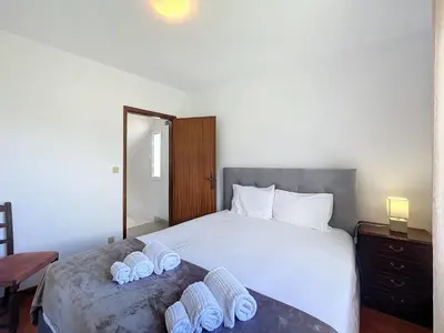 a bedroom with a large white bed with two pairs of slippers at Casa do Romaninho in Porto da Cruz