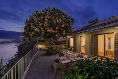 a house with a table and a tree next to the water at Lazareto Mar by An Island Apart in Funchal