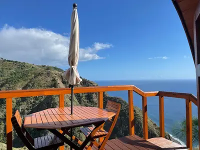 a patio with an umbrella and a table and chairs at The tiny black bird in Fajã da Ovelha
