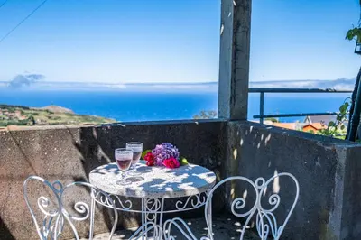 a table with two glasses and flowers on a balcony at Rainbow Cottage by Homie in Ponta do Pargo