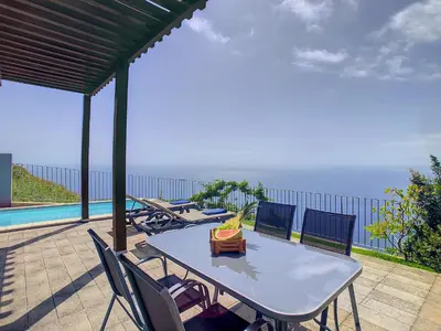 a table and chairs on a patio with a view of the ocean at Villa Miradoura by LovelyStay in Arco da Calheta