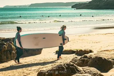 two people walking on the beach with a surfboard at Wayra Lodge [Kanchay] in Raposeira