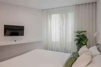 a white room with a white bed and a tv at Cine Park Residences by An Island Apart in Funchal