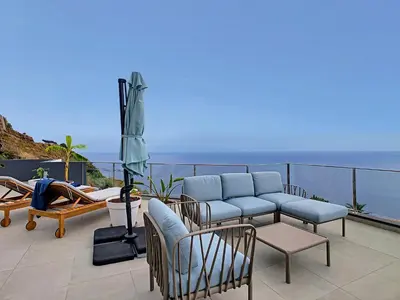 a patio with chairs and an umbrella and the ocean at Villa Omar by LovelyStay in Canhas
