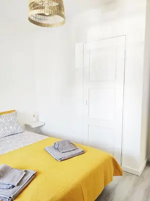 a white bedroom with a yellow bed and a chandelier at Caroline's in Vila do Bispo