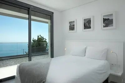 a bedroom with a white bed and a large window at SKYFALL VILLA in Arco da Calheta