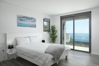 a white bedroom with a bed and a large window at SKYFALL VILLA in Arco da Calheta