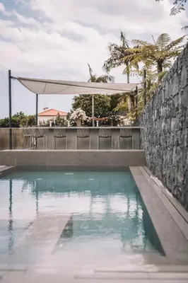 a swimming pool with a table and chairs next to a wall at VILLA QUINTA TORRINHA Rooms in Funchal