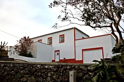 a white house with red doors and a stone wall at Casa de Almagreira - Empreendimento de Turismo em Espaço Rural - Casa de Campo in Vila do Porto