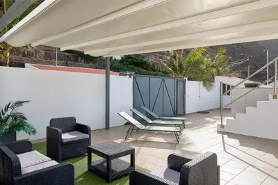 a patio with chairs and tables and an umbrella at villa com piscina entre o mar e as montanhas in Paul do Mar