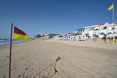 a beach with a yellow and red flag and some buildings at 413 Casa Marsalema in Salema