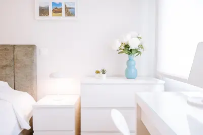 a white bedroom with a vase of flowers on a table at Apartamento Feliz by Amazing Madeira in Funchal
