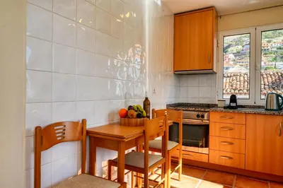 a kitchen with a wooden table and chairs and a table and a bowl of fruit at Largo dos Milagres, a Home in Madeira in Machico