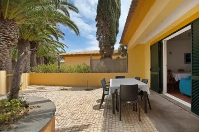 a table and chairs on a patio with palm trees at Casa de férias a 75 metros da praia in Campo de Baixo