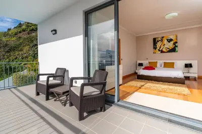 a bedroom with a balcony with a bed and chairs at Villa Nunes, Big Holiday house with private pool in Calheta