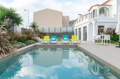 a pool with chairs and a table and a house at Casa Paul do Mar in Paul do Mar