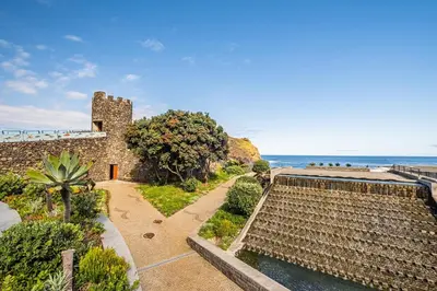 a building with a garden and the ocean in the background at Porto Moniz City Centre by Homie in Porto Moniz