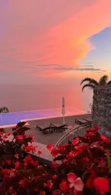 a sunset over a pool with red flowers at Ocean View Madeira 1 - Ponta do Sol in Canhas