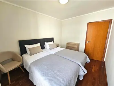 a bedroom with a large white bed and a chair at Wings Apartment in Santa Cruz