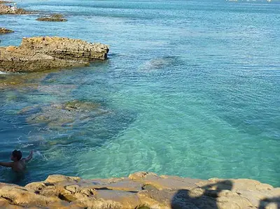 a man swimming in the water near some rocks at The Secret Corner of Luz in Luz