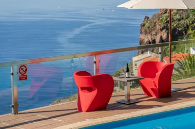 two red chairs and a table on a balcony overlooking the ocean at OurMadeira - Vista Grande in Caniço
