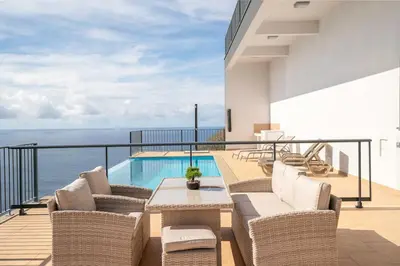a balcony with chairs and a table and a pool at Marina View Apartment - Pool & stunning ocean view in Calheta