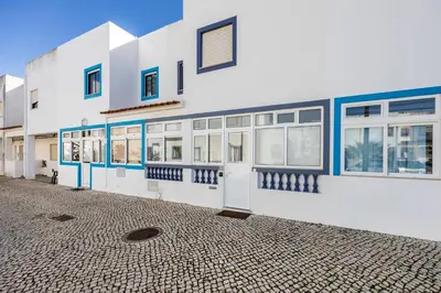a white building with blue windows and a cobblestone street at Bay View Townhouse in Salema
