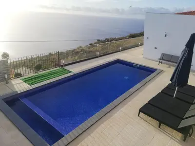 a blue swimming pool with a view of the ocean at Majestic Seaview Villa in Fajã da Ovelha
