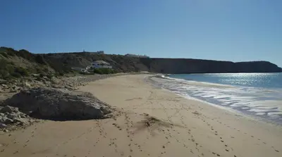 a beach with footprints in the sand and water at Casa Sagres T2 - 3 minutos a pé Praia da Mareta in Sagres