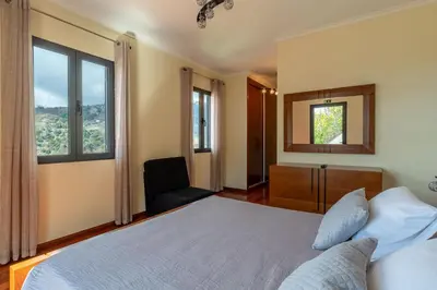 a bedroom with a bed and a chair and windows at Gran Horizonte House by Holiday Rental Madeira in Ribeira Brava
