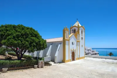 a church with a clock tower next to the ocean at Villa Camena, private pool, sea view, residential area outside of the village Praia da Luz in Luz