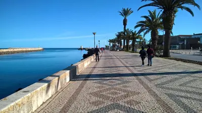 people walking down a sidewalk next to the water at Villa Camena, private pool, sea view, residential area outside of the village Praia da Luz in Luz