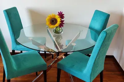 a glass table with chairs and a vase with a sunflower on it at Jardim Sol Holiday Apartment in Funchal