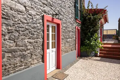 a stone building with a white door and red trim at Corman House, Sea View & Pool in Arco da Calheta
