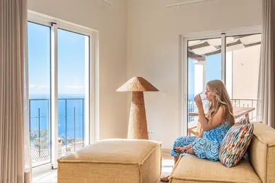a woman sitting on a chair in a room with a window at Villa Sea Renity - Palheiro Village by ALMA Holiday Rentals in Funchal