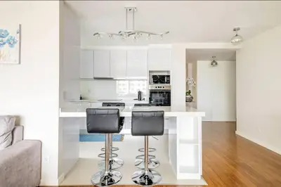 a white kitchen with a counter and two bar stools at Luxury poolside view apartment in Funchal