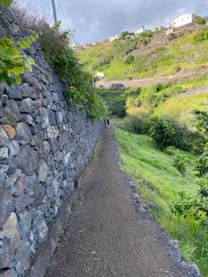 a stone wall next to a path next to a hill at Tranquilidade in Estreito da Calheta