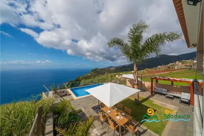 a patio with a table and a white umbrella at OurMadeira - OceanScape in Madalena do Mar