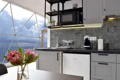 a kitchen with white cabinets and a table with a vase of flowers at Vi Naturae Glamping in Fajã da Ovelha