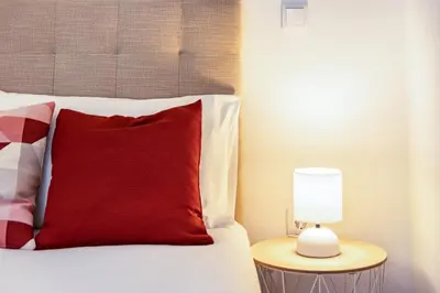 a bed with a red pillow and a lamp on a table at Casa do Porto in Paul do Mar
