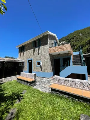 a stone house with a hill in the background at Casa da Nogueira in Porto Moniz