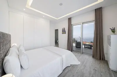 a white bedroom with a bed and a large window at Villa Calhetascape by Villa Plus in Estreito da Calheta